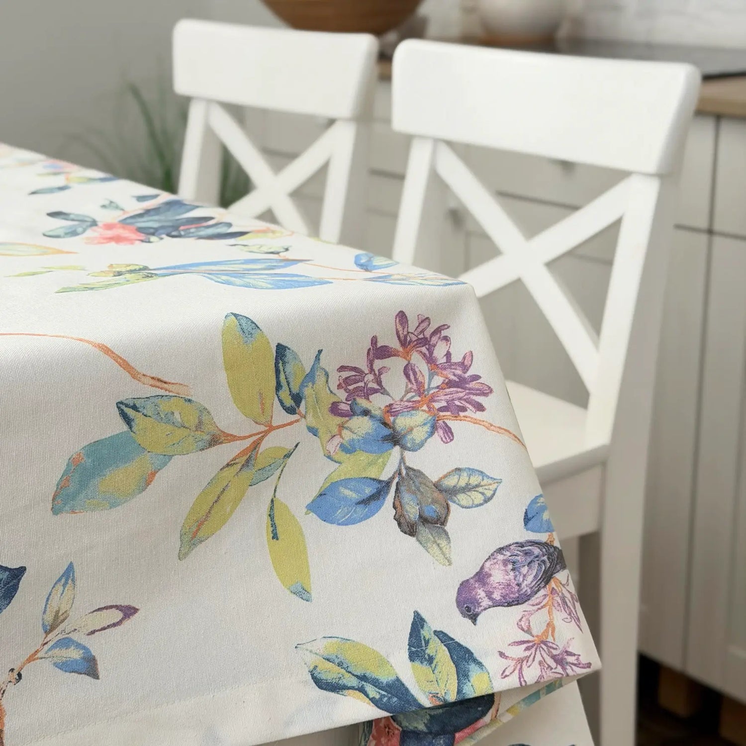 Tablecloth with colorful floral design on a table with white chairs.