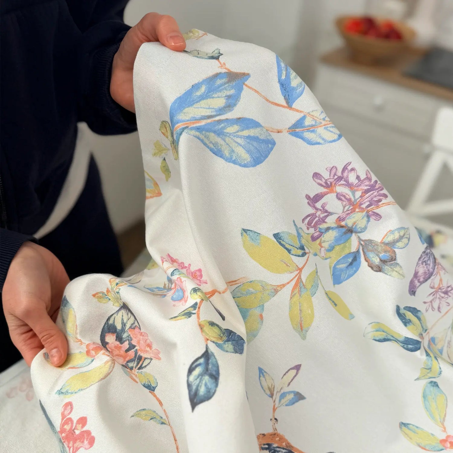 Person holding fabric with colorful floral pattern in a kitchen setting
