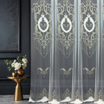 Decorative sheer curtains with gold embroidery in a room setting.