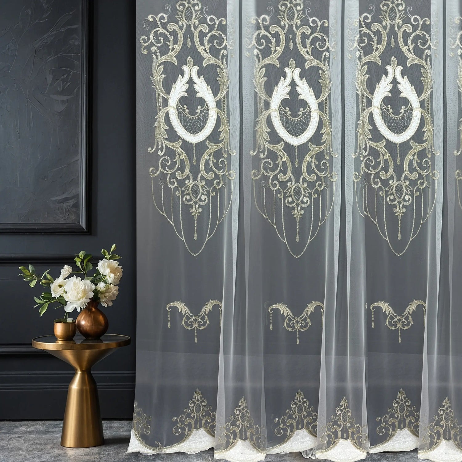 Decorative sheer curtains with gold embroidery in a room setting.