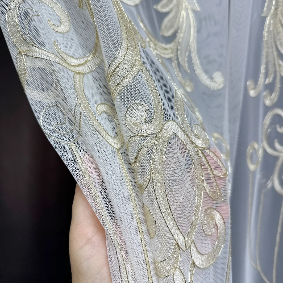 Close-up of a hand holding sheer fabric with gold embroidery against a dark background