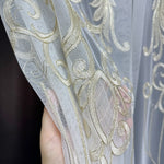 Close-up of a hand holding sheer fabric with gold embroidery against a dark background