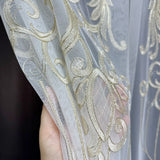 Close-up of a hand holding sheer fabric with gold embroidery against a dark background