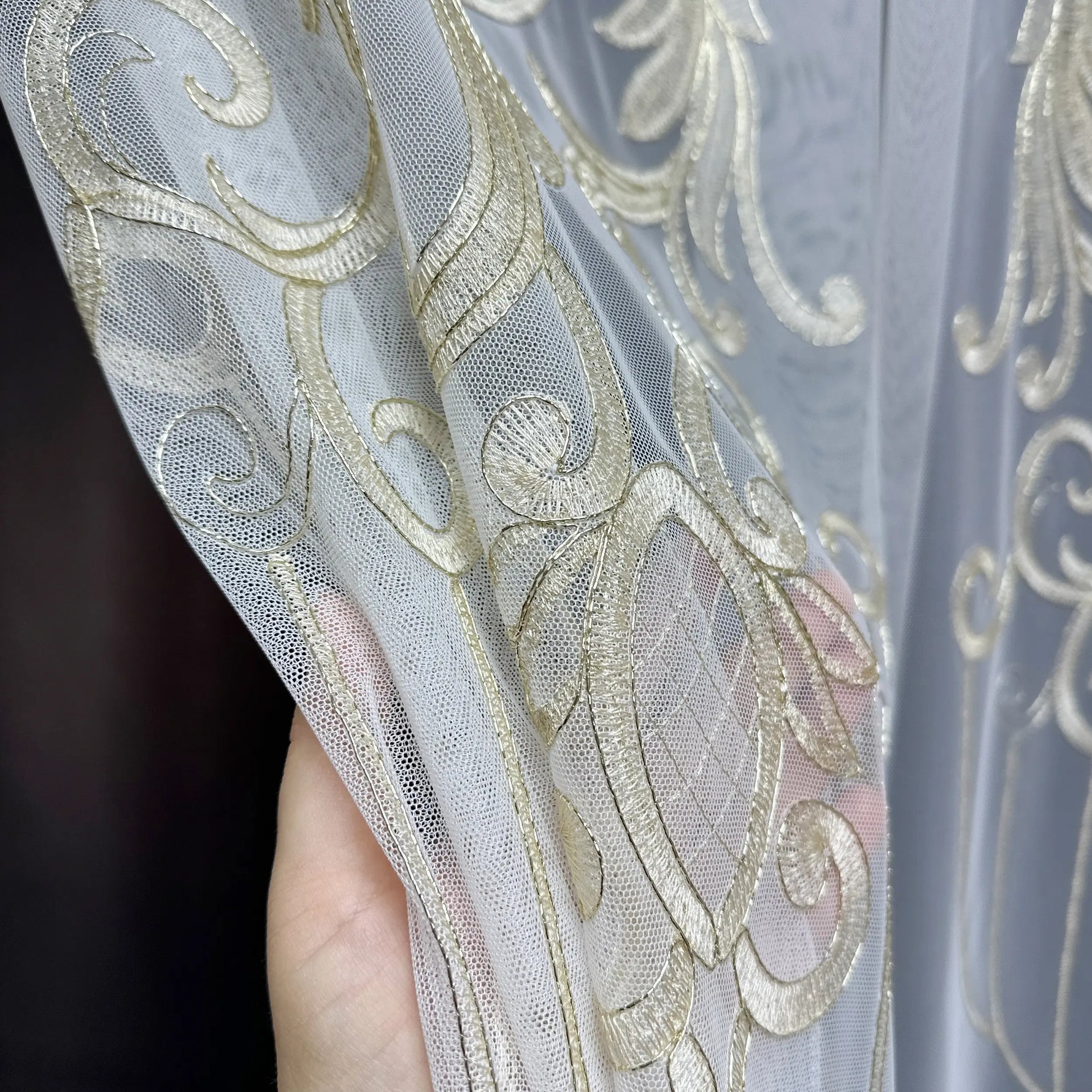 Close-up of a hand holding sheer fabric with gold embroidery against a dark background