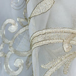 Close-up of a sheer fabric with intricate gold embroidery on a light gray background