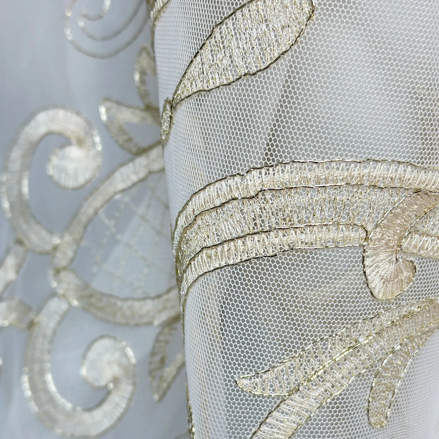 Close-up of a sheer fabric with intricate gold embroidery on a light gray background