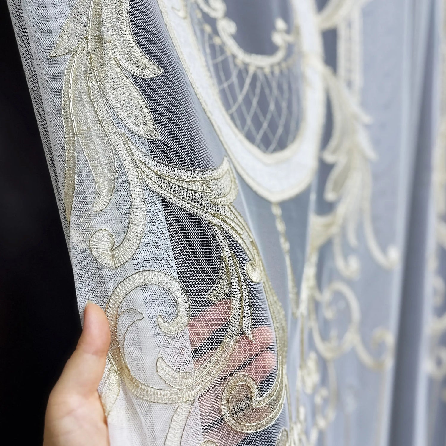 Decorative fabric with gold embroidery held by a hand against a dark background