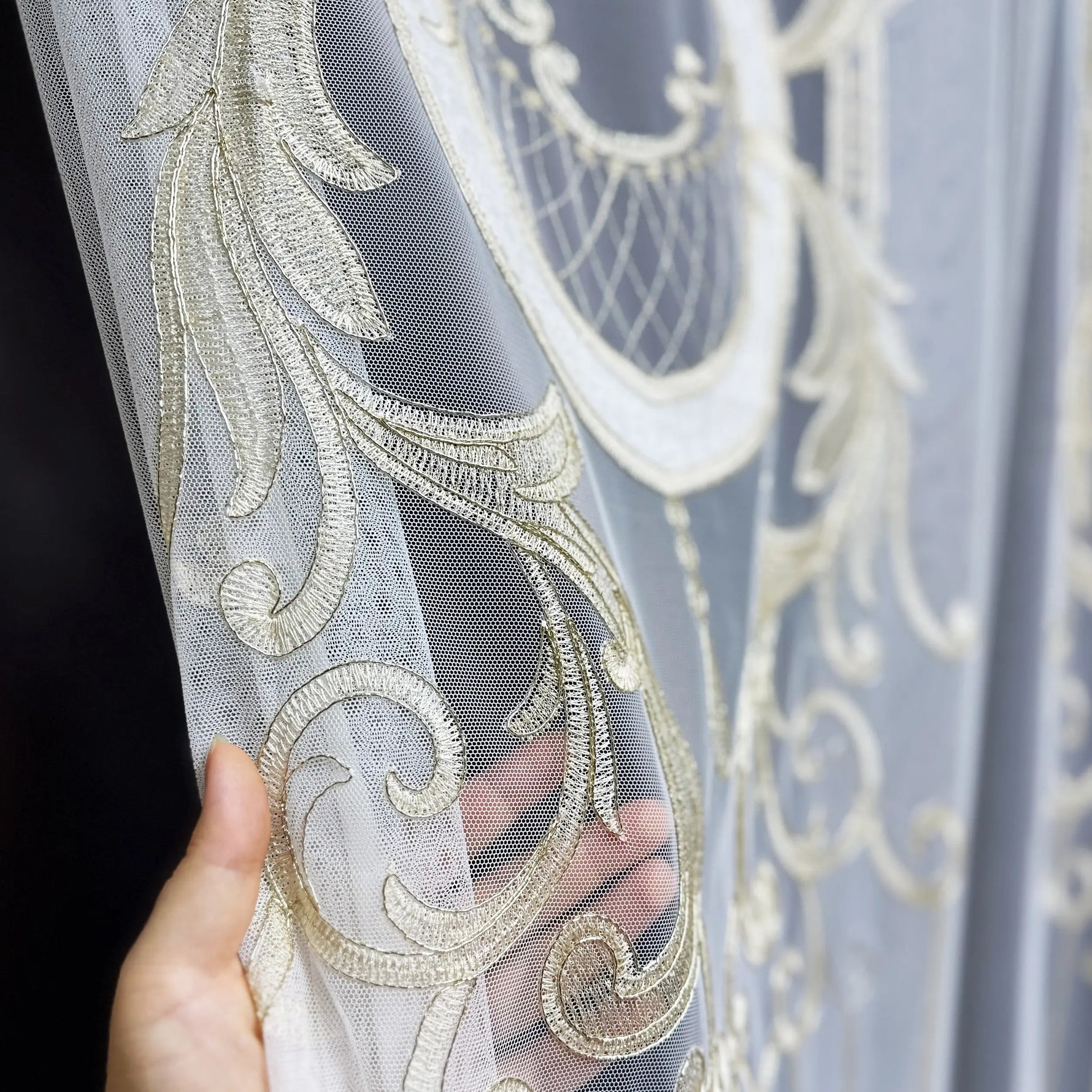 Decorative fabric with gold embroidery held by a hand against a dark background