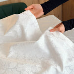 Person holding a piece of white lace fabric with a blurred background