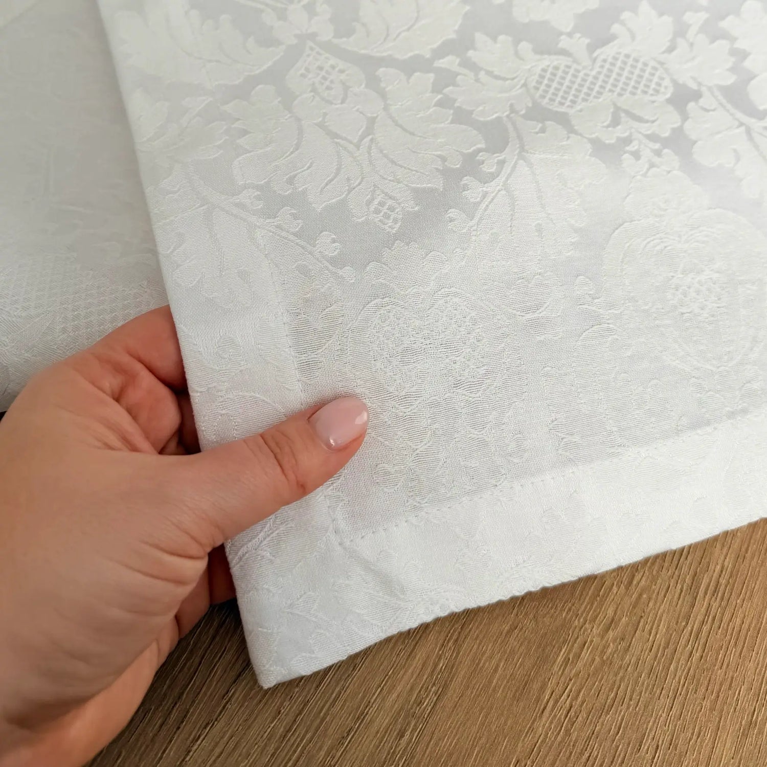 Hand holding a sheet of white lace fabric on a wooden surface