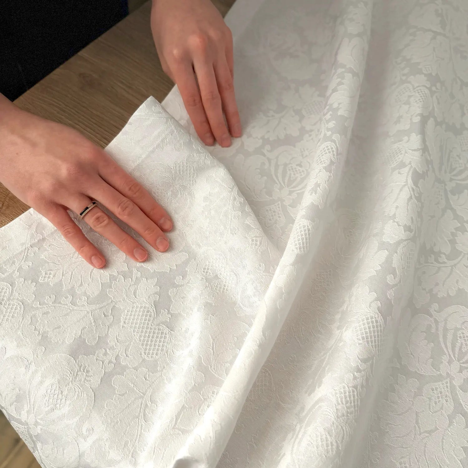 White lace fabric with hands smoothing it out on a wooden surface