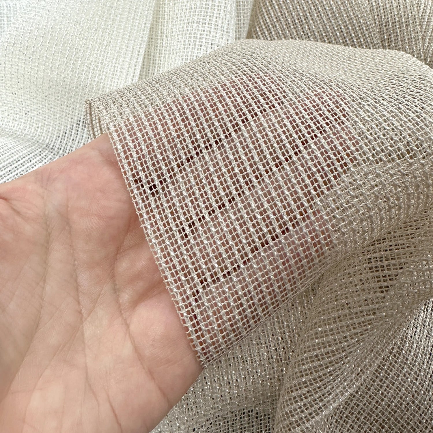 Close-up of a hand holding a piece of mesh curtains fabric.