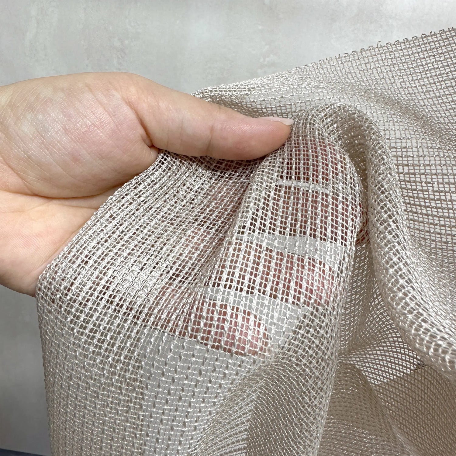 Hand holding a piece of beige mesh fabric of anti claw curtains