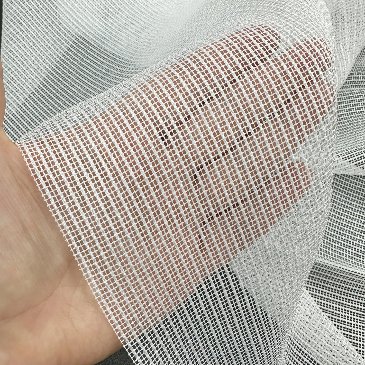 Close-up of a hand holding a piece of white mesh curtains fabric.