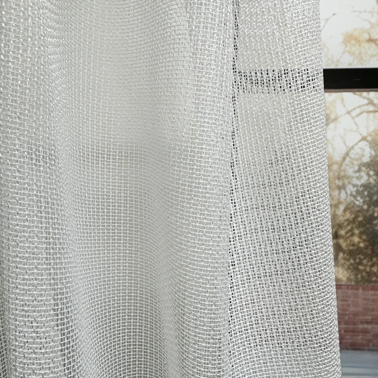 Close-up of a textured white curtain with a blurred outdoor background