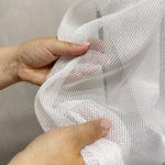 White mesh curtains fabric held by hands against a neutral background