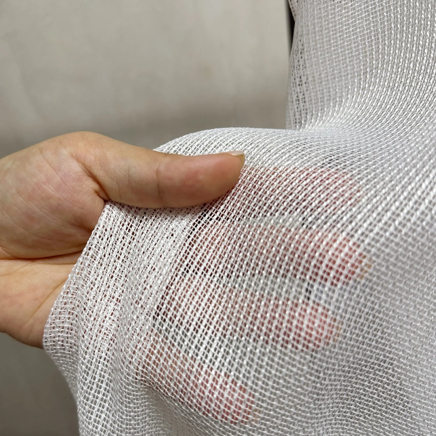 Close-up of a hand holding a piece of white mesh sheer curtains fabric.