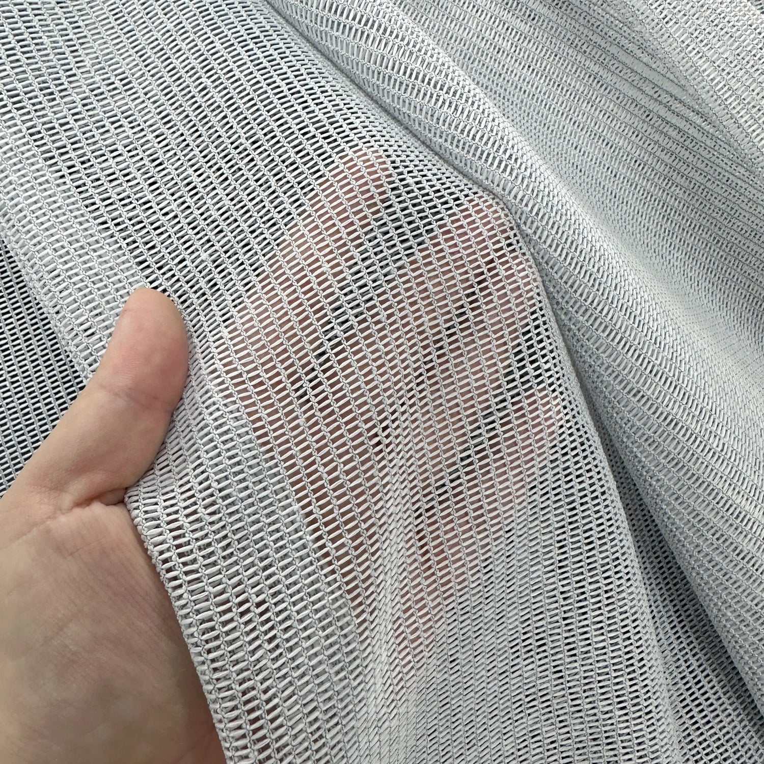 Close-up of a hand holding a piece of textured gray curtains fabric.