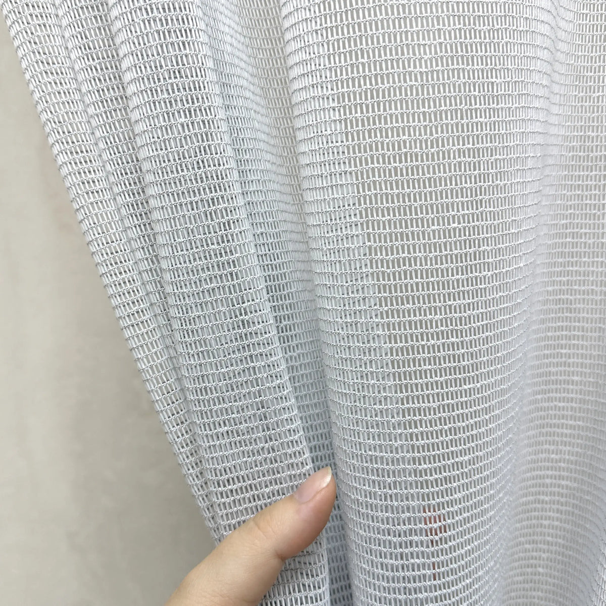 Close-up of a hand holding a piece of textured gray curtains fabric against a neutral background