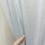 Close-up of a hand holding a piece of textured gray curtains fabric against a neutral background