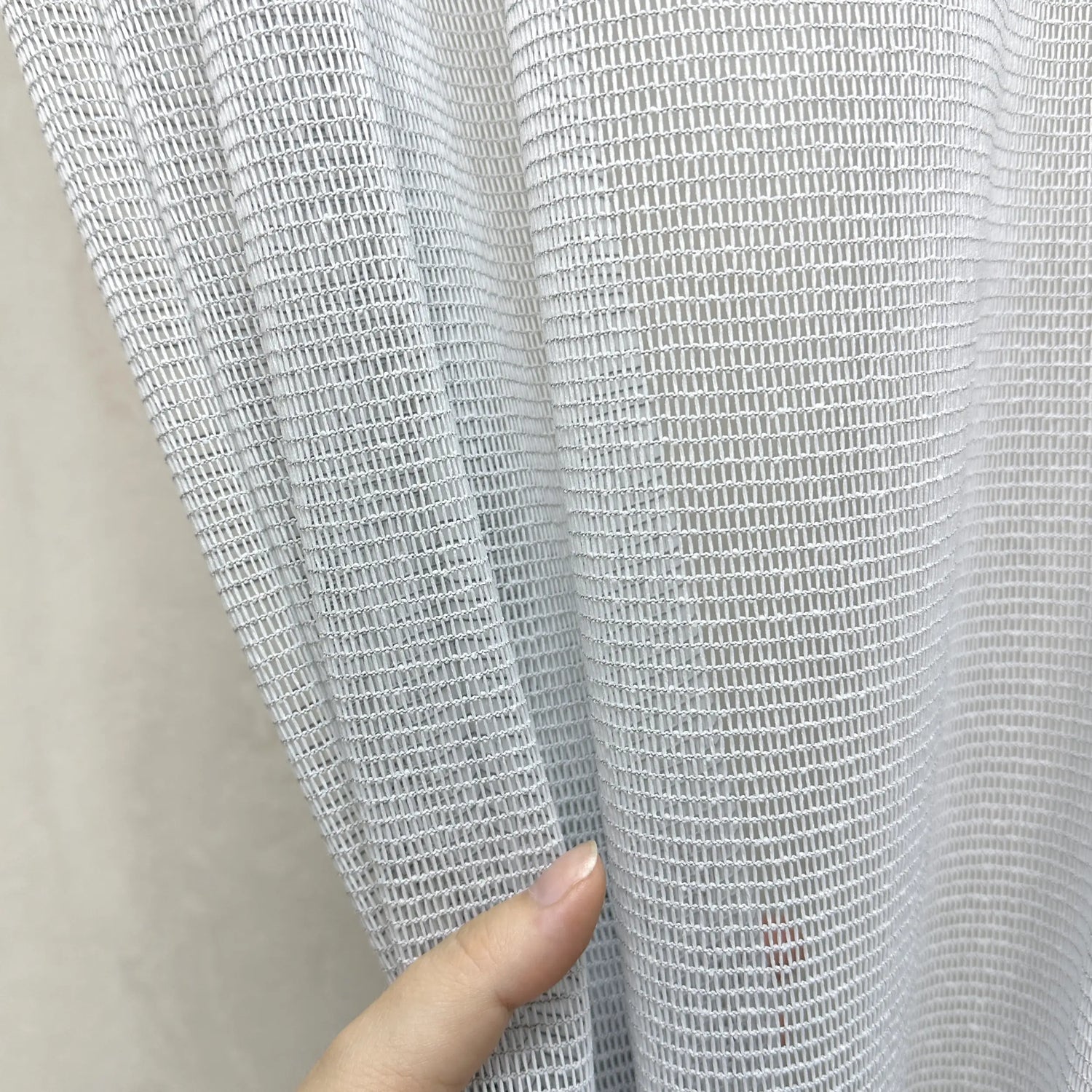Close-up of a hand holding a piece of textured gray curtains fabric against a neutral background