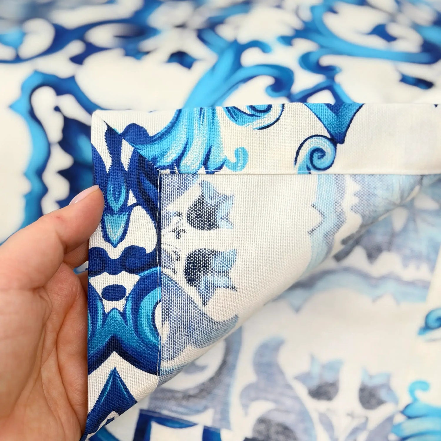 Close-up of a hand holding fabric with blue and white pattern, showing a patch of plain white fabric.